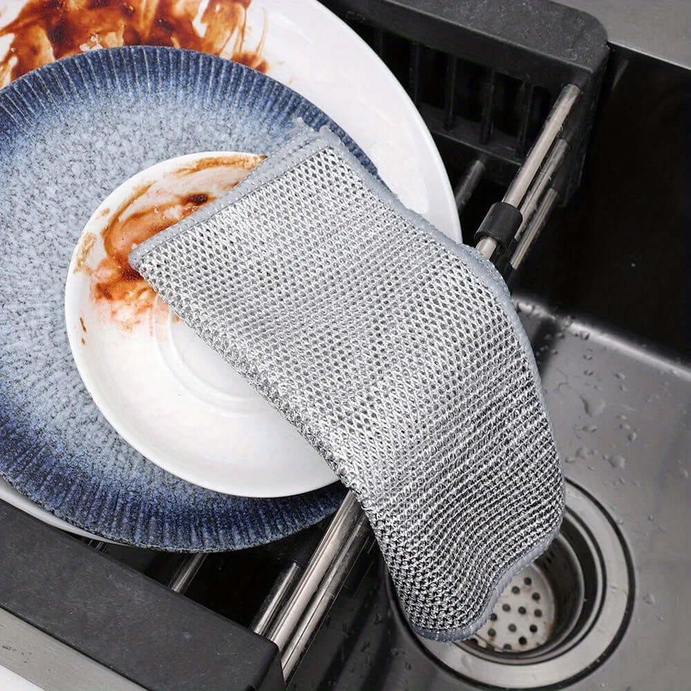 12pcs non-stick oil iron dishwashing cloths resting beside dirty plates in kitchen sink for efficient cleaning.