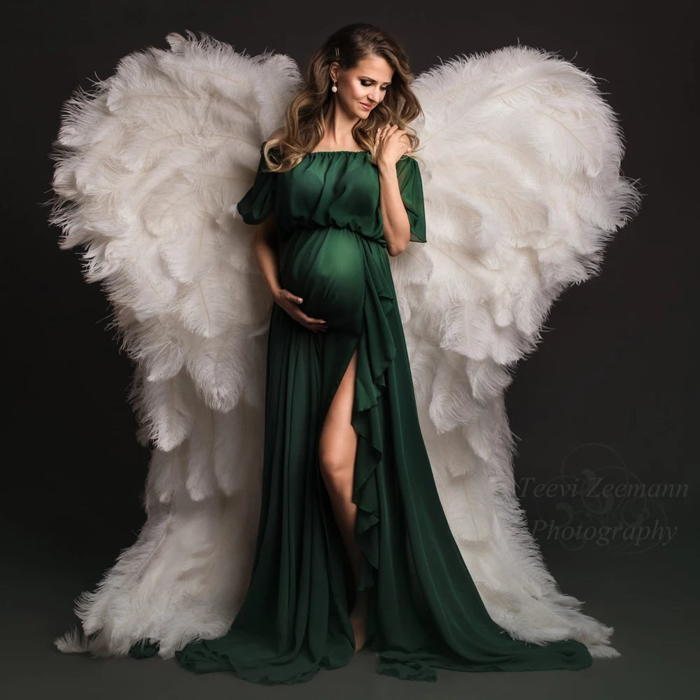 Maternity model in a green chiffon ruffle sleeve dress with angel wings backdrop, showcasing summer elegance.