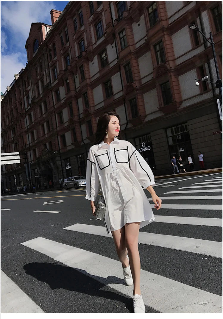 Woman in a white shirt dress with pockets walking on a city street, showcasing a stylish summer outfit.