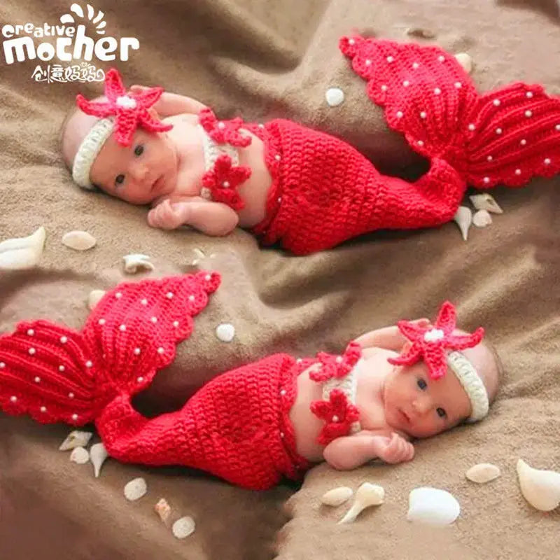 Adorable unisex infant in a red crochet mermaid costume on a sandy surface, perfect for newborn photography.