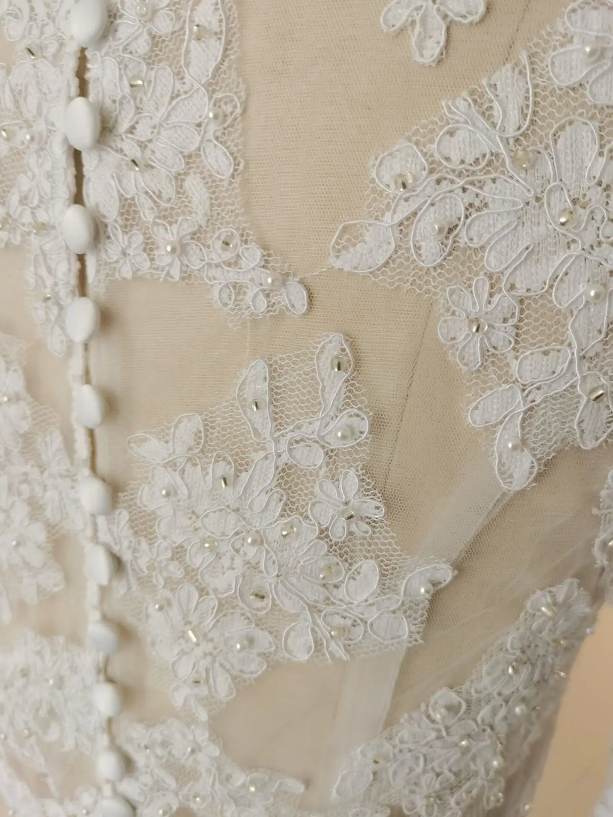 Close-up of crystal beaded wedding jacket fabric featuring intricate lace appliqué and button details.