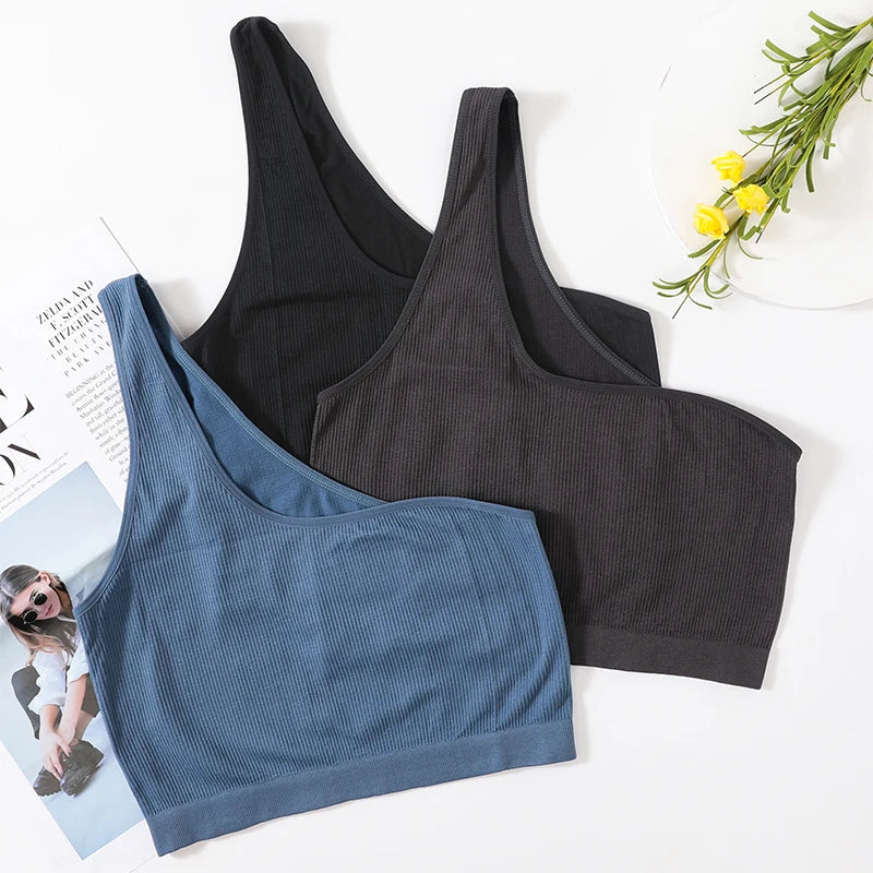 Three colors of MonoSculpt™ One-Shoulder Seamless Crop Tops displayed with a magazine and flowers.