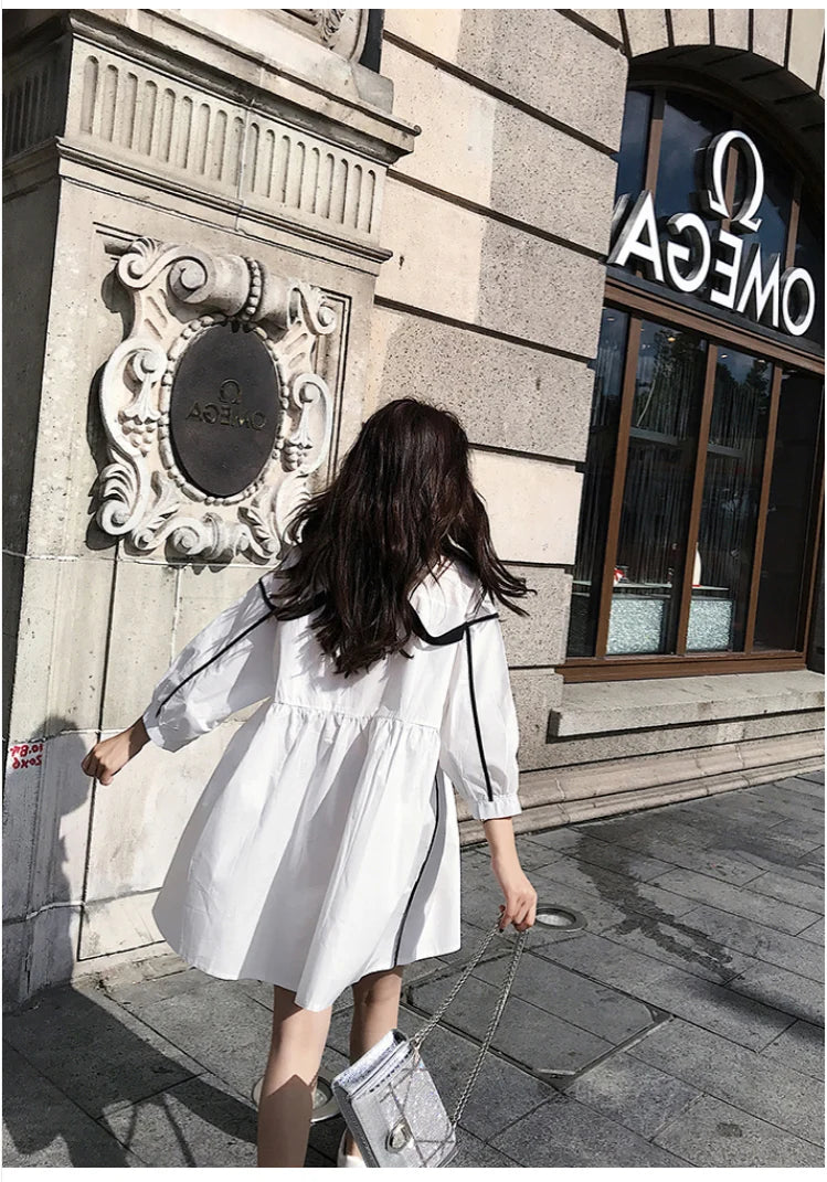 Back view of a woman wearing a white solid color maternity shirt dress with a turn-down collar.