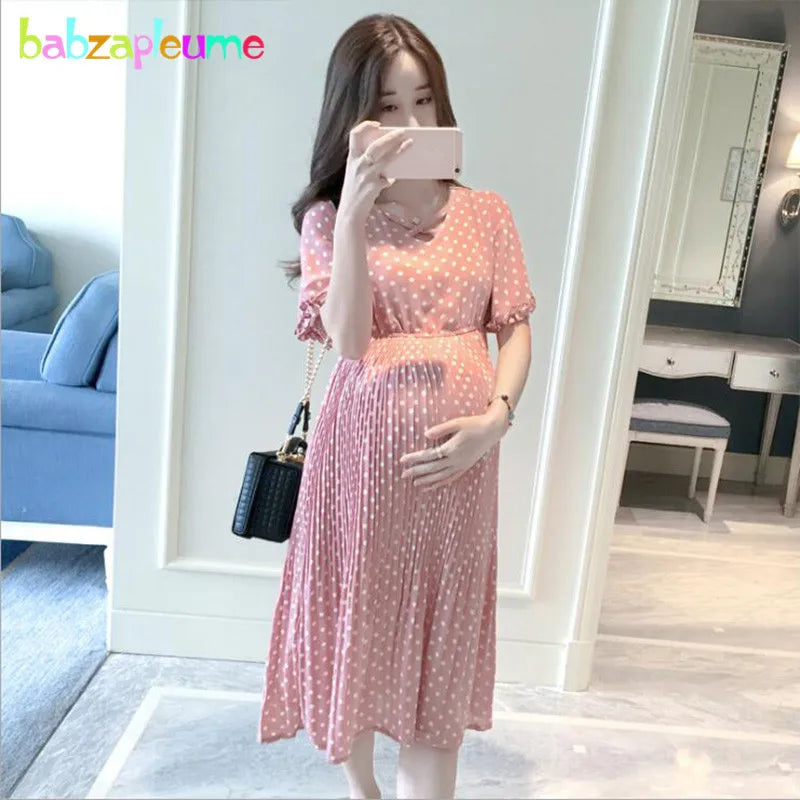 Woman in a pink chiffon polka dot maternity dress, showcasing a casual summer style.