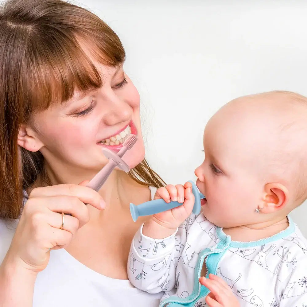 Mother and baby using soft silicone training toothbrushes for infants' oral care.