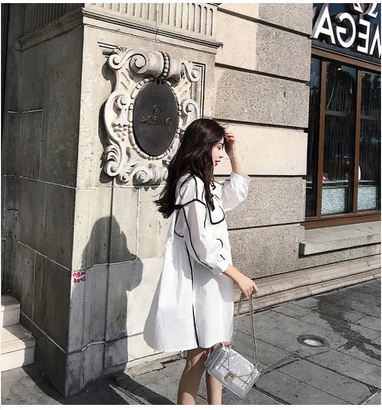 Woman wearing a solid color maternity shirt dress, posing outside a building with stylish architecture.