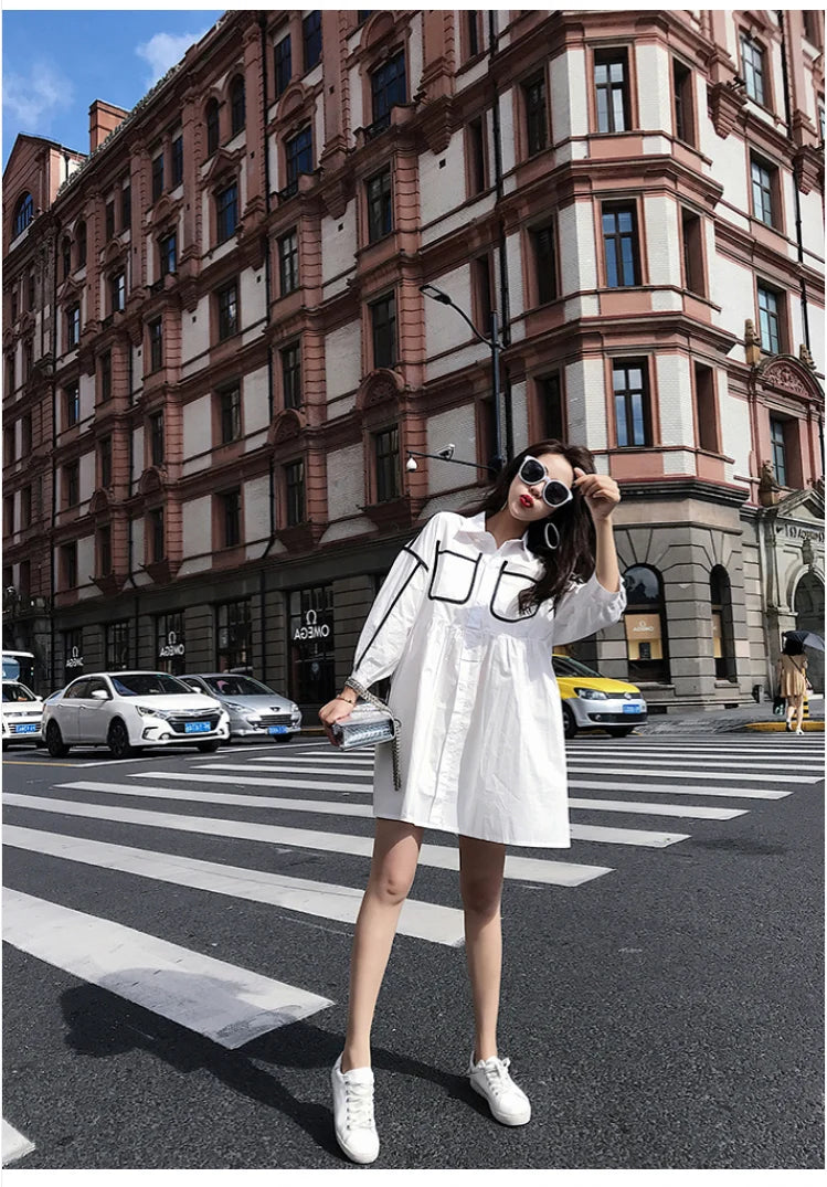 Woman wearing a solid color maternity shirt dress, posing stylishly on a city street.