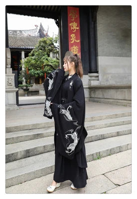 Woman wearing a Han Dynasty couple costume in black with dragon embroidery, posing outdoors near a traditional building.