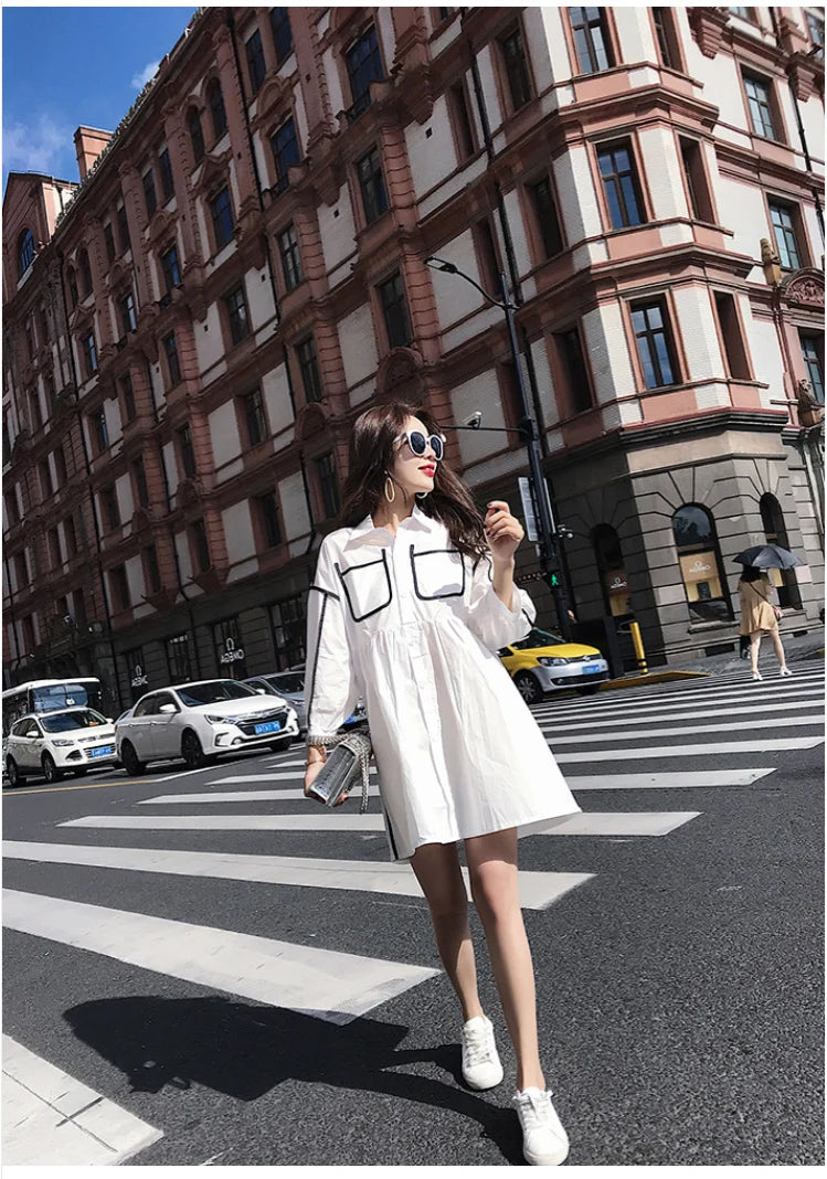 Model wearing a solid color maternity shirt dress with pockets, enjoying a summer day on a busy city street.