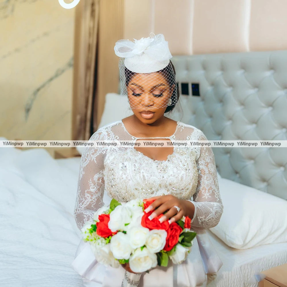 Bridal model wearing an African lace wedding dress with a crystal beaded design, holding a bouquet of red and white flowers.
