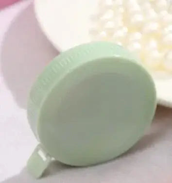 Green circular measuring tape on a pink background, ideal for sewing and crafting.