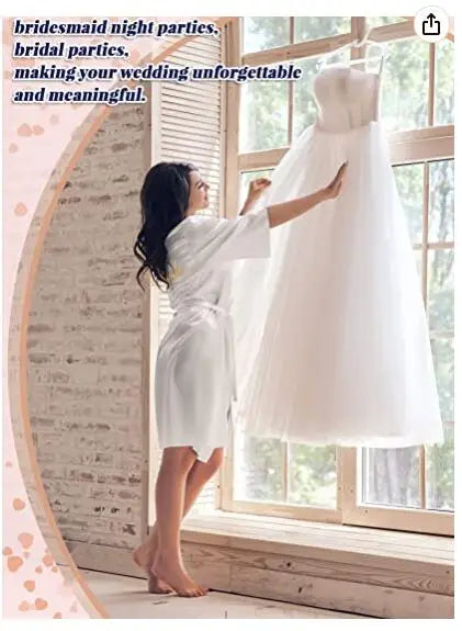 Woman in a white satin robe admiring a bridal dress by a window, perfect for bridesmaid or bridal parties.
