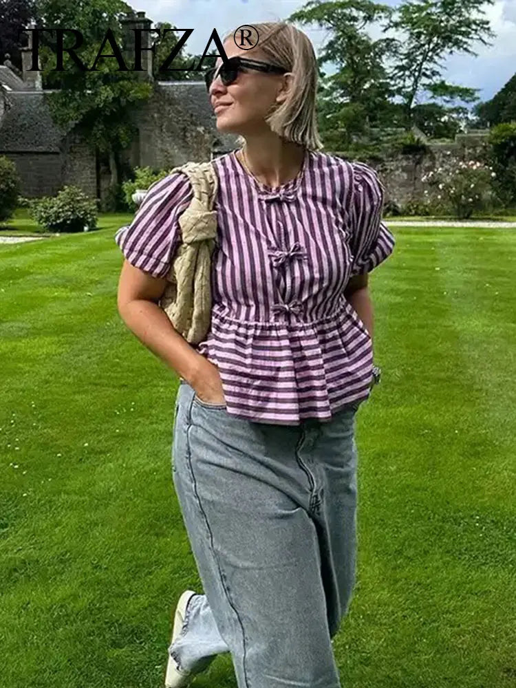 Woman in TRAFZA striped lace-up blouse, enjoying outdoor scenery, showcasing short sleeves and a stylish casual look.
