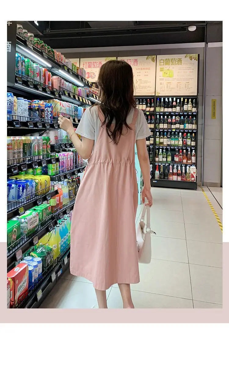 Woman wearing a pink loose fit maternity dress in a store aisle with beverages.