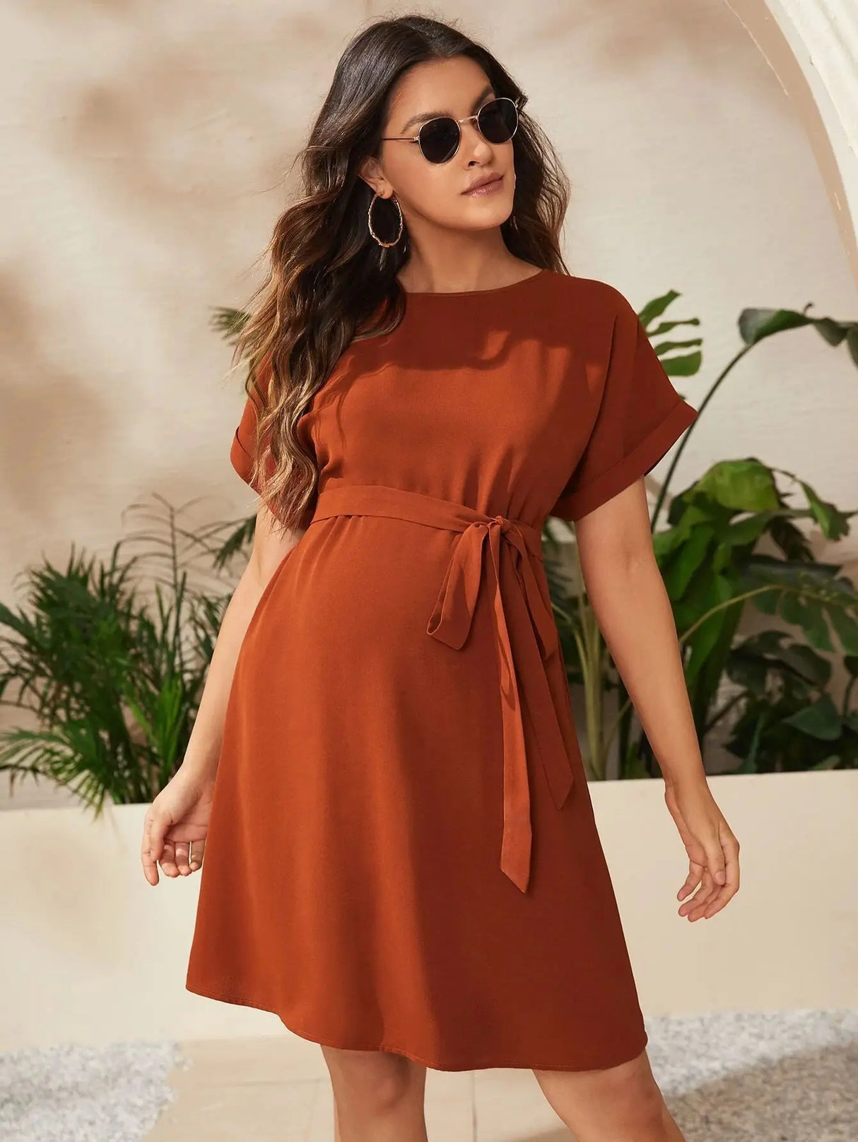 Stylish woman in a brown bat-sleeve maternity tunic dress, perfect for summer photoshoot with a natural background.