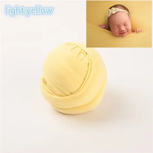Light yellow baby blanket shoot backdrop with a cozy infant wrap and adorable sleeping baby.