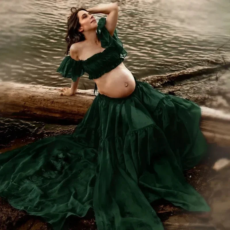 Maternity photoshoot featuring a woman in a boho two-piece green chiffon set by a river.