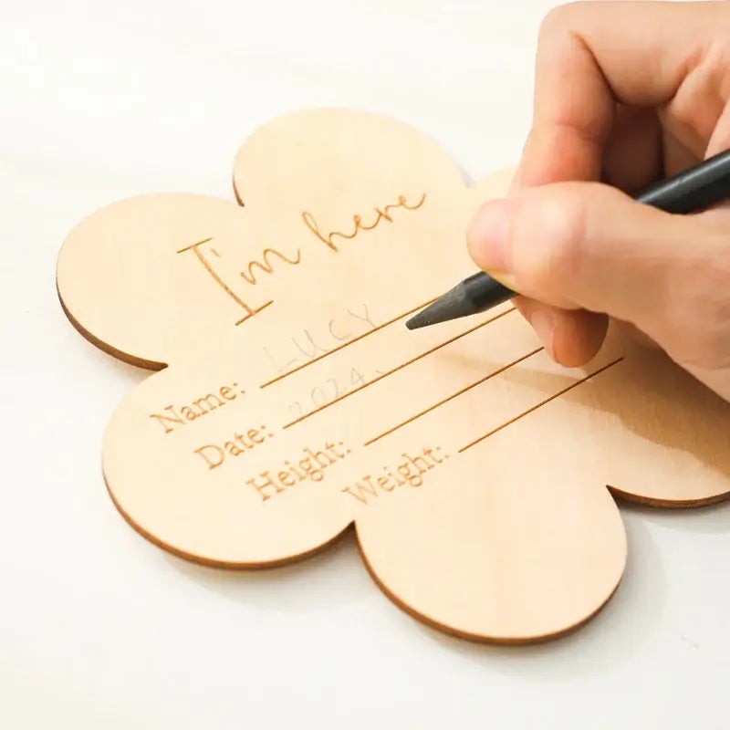 A wooden flower-shaped milestone plaque being personalized with a name and date for a baby.