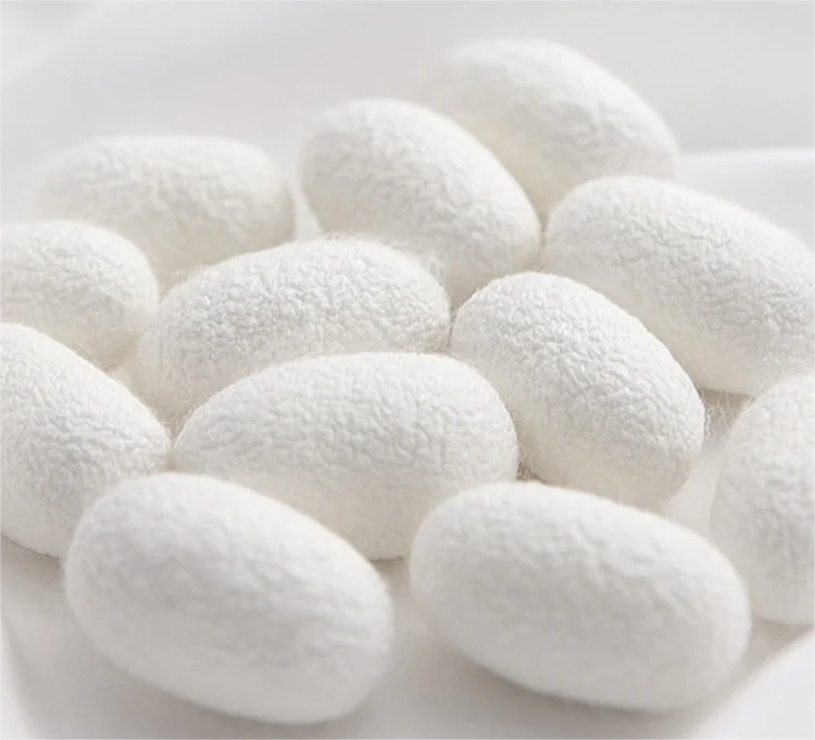 Close-up of white silk cocoons on a pale background, showcasing their soft texture and natural form.