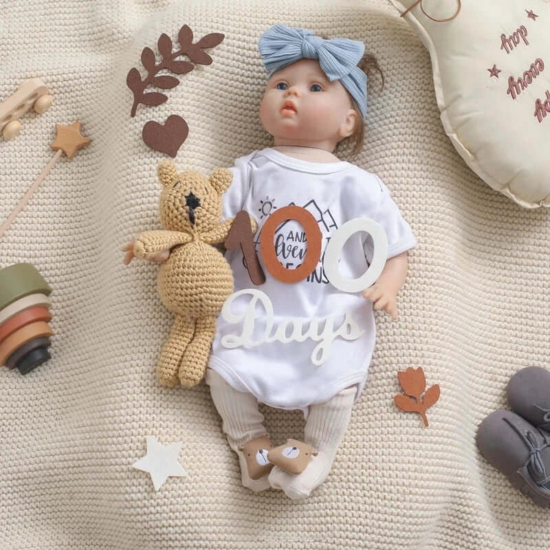 Baby doll with milestone card, soft toy, and decorative elements on a cozy knit blanket.