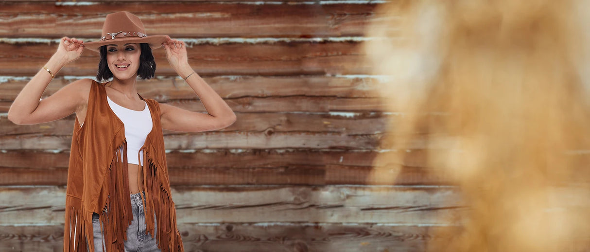 Woman wearing a cowboy costume with a tassel vest and hat, showcasing a fun western style against a rustic backdrop.