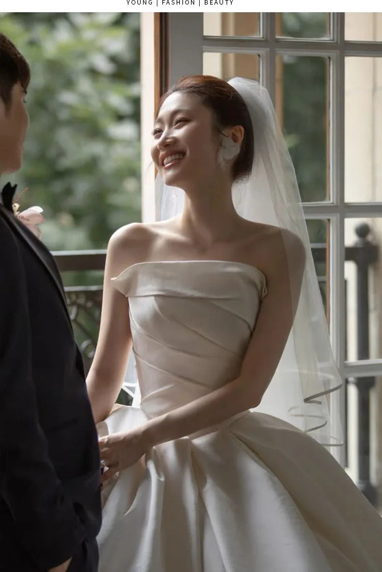 Bride in a strapless satin wedding gown smiling at her partner, showcasing a beautiful bridal look with a veil.