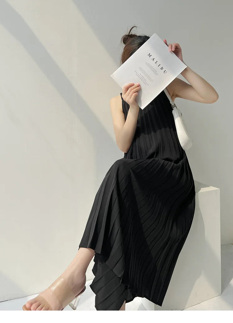 Model wearing a pleated black chiffon maternity dress, mid-calf length, holding a magazine, showcasing a casual summer style.