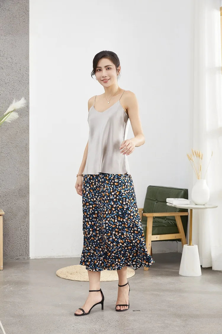 Woman in a silk camisole and floral skirt, showcasing summer fashion in a stylish indoor setting.