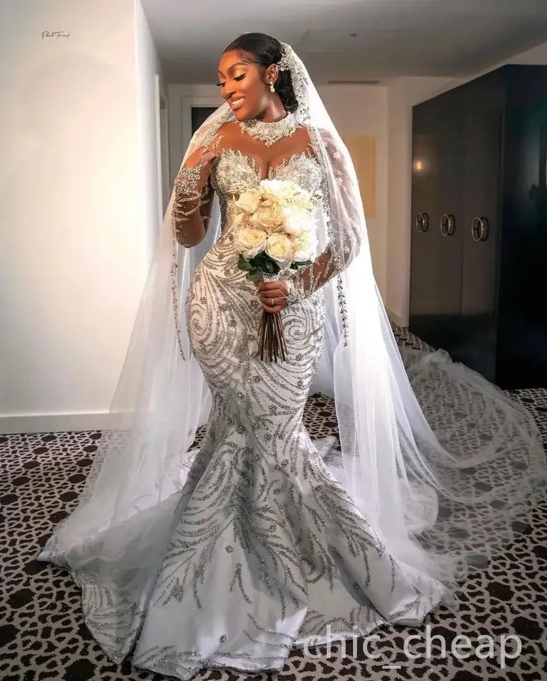 Elegant bride in a luxurious mermaid wedding dress with beaded sheer sleeves, holding a bouquet of roses.