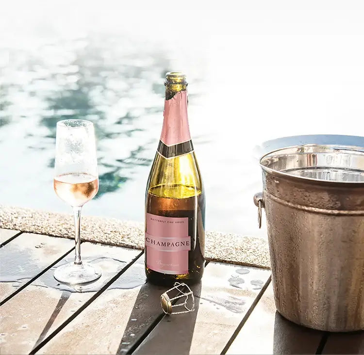 Chilled rose champagne bottle with a glass beside a pool, creating a luxurious outdoor setting.