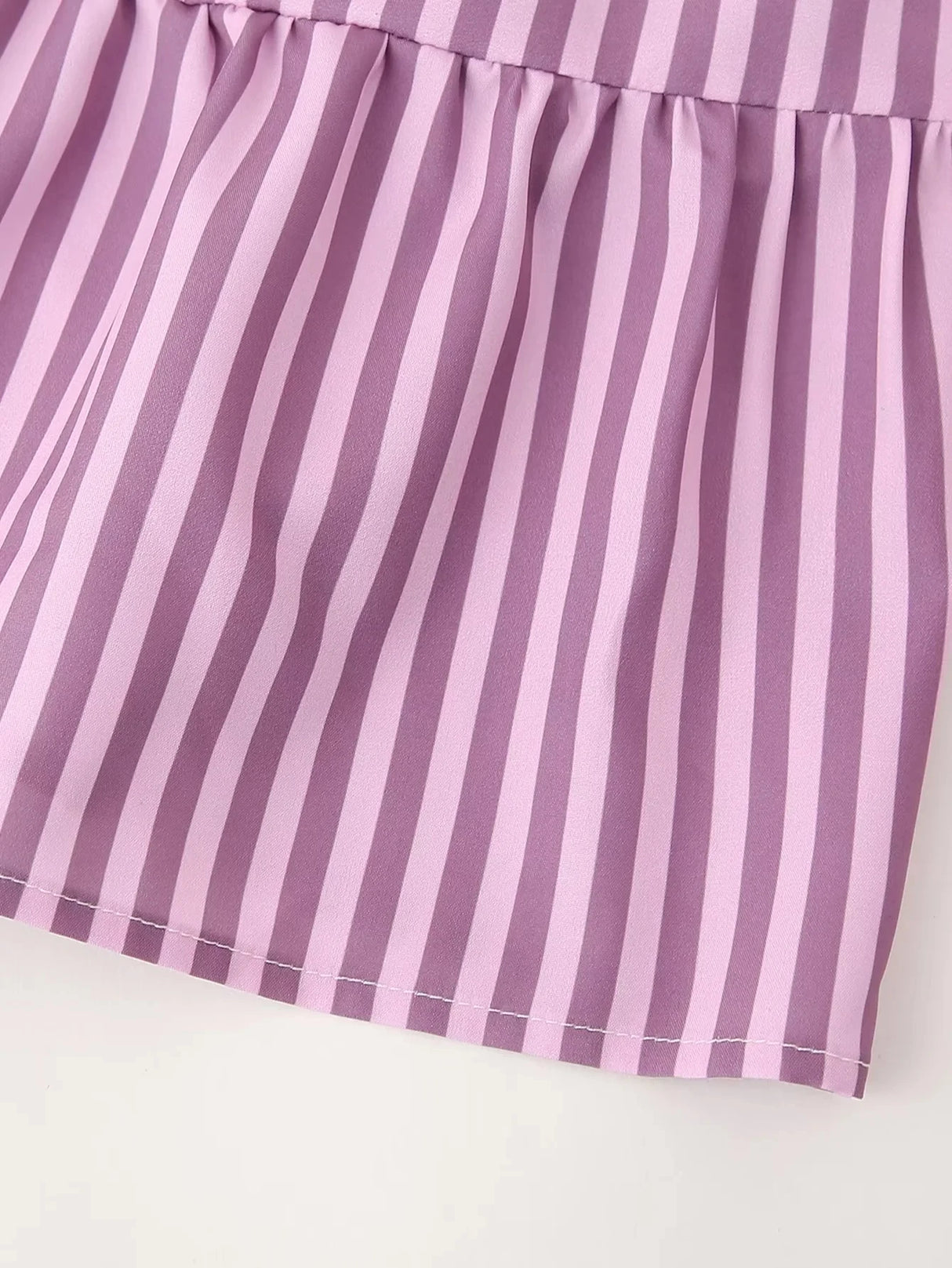 Close-up of the BowChic™ stripe lace-up blouse in soft lavender color with elegant pleated bottom.