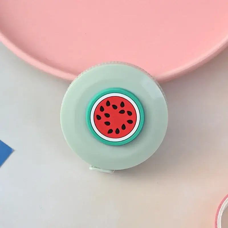 Colorful watermelon-themed tape measure resting on a pastel pink surface, perfect for cute home decor and measurements.