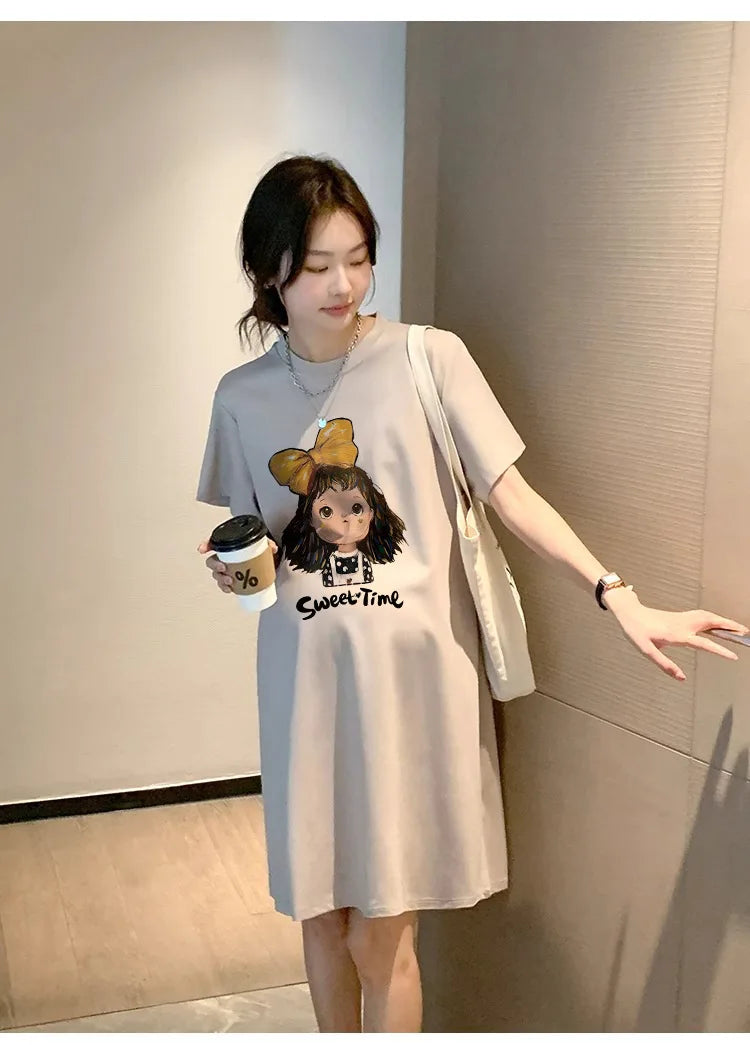 Model wearing a loose-fitting, knee-length casual maternity t-shirt dress featuring a cartoon design and boat neck.
