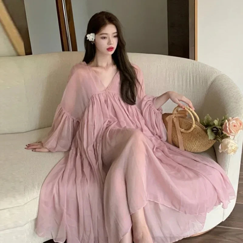 Elegant woman in a pink strappy maternity dress, styled casually for summer, sitting on a sofa with a handbag.