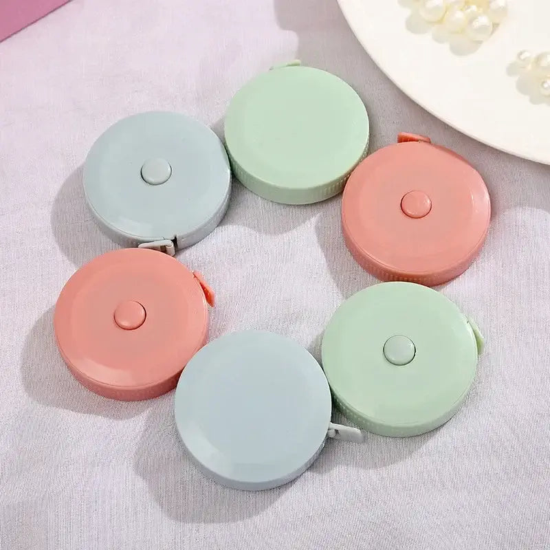 Colorful round tape measures in pastel green, blue, and pink arranged on a fabric surface.