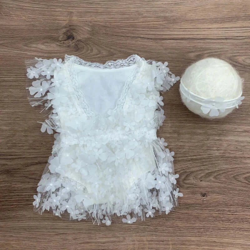 Newborn photography prop featuring a white floral baby romper and a soft decorative ball, perfect for unisex photo sessions.