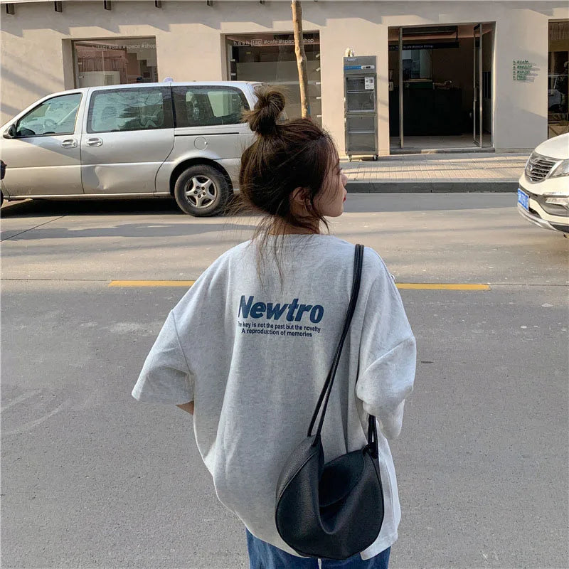 Woman wearing an oversized gray Harajuku streetwear tee with 'Newtro' print, strolling down a city street.