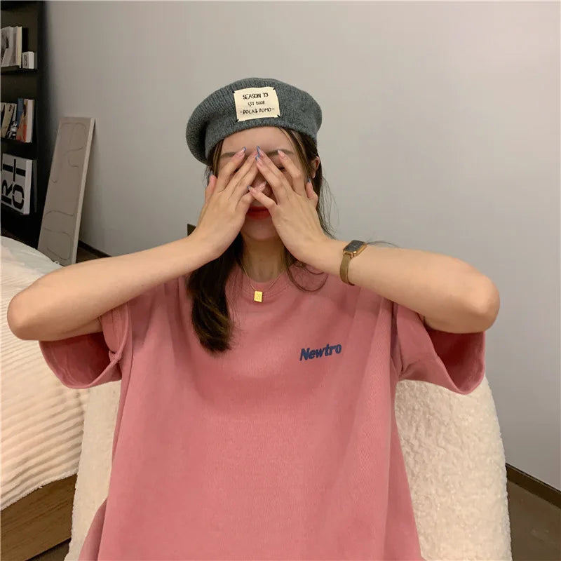 Woman wearing a pink oversized Harajuku streetwear tee with Newtro print and a gray beret, posing playfully indoors.