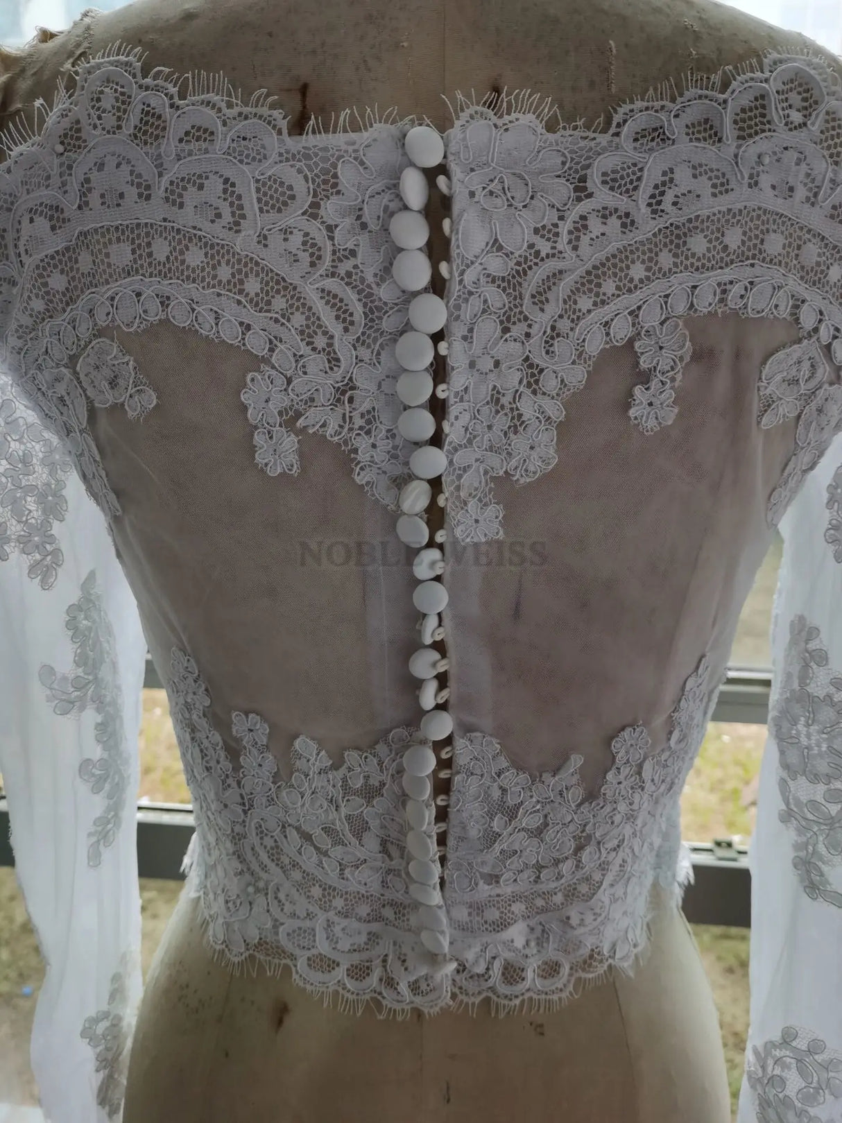 Close-up of the back of a Lace Off Shoulder Bridal Jacket with intricate appliqued lace and button details.