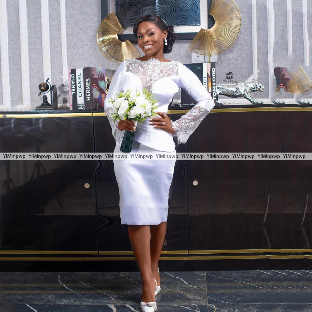Elegant bride in a satin tea-length gown with lace sleeves, holding a bouquet, standing in a stylish modern room.