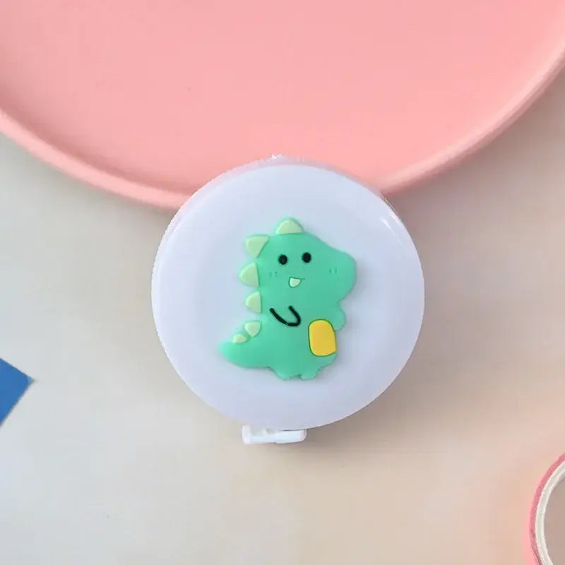 Cute green dinosaur tape measure on a white casing, ideal for kids' height measurement and playful decor.