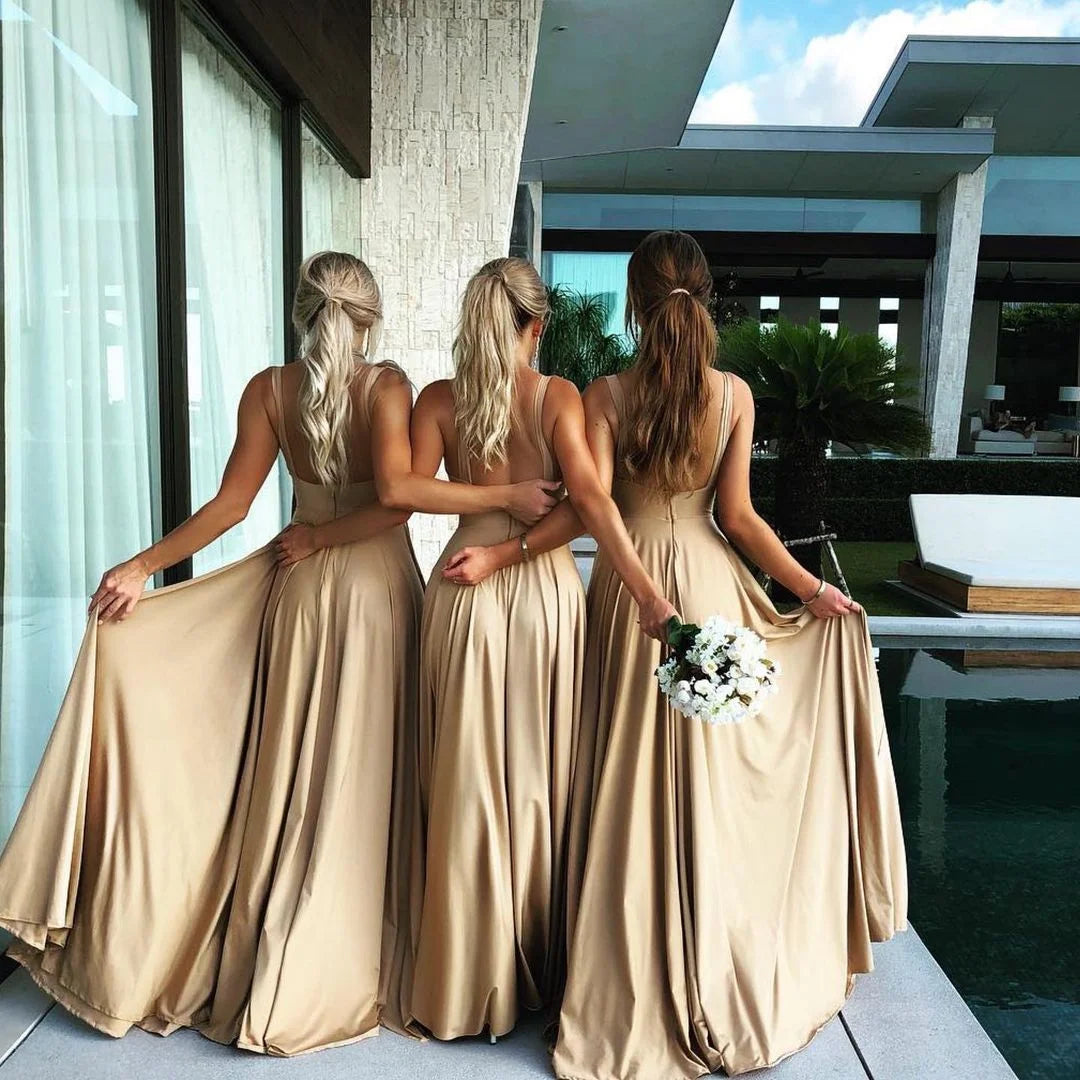 Three bridesmaids in elegant floor-length V-neck gowns holding skirts, showcasing a backless design.