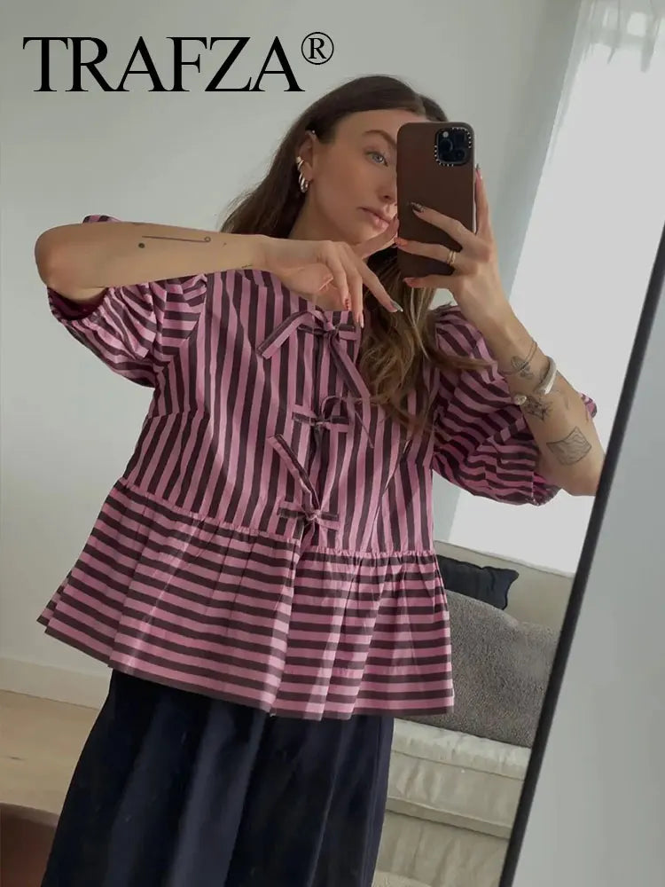 Woman modeling a TRAFZA stripe lace-up blouse in pink and black, showcasing short sleeves and a relaxed fit.