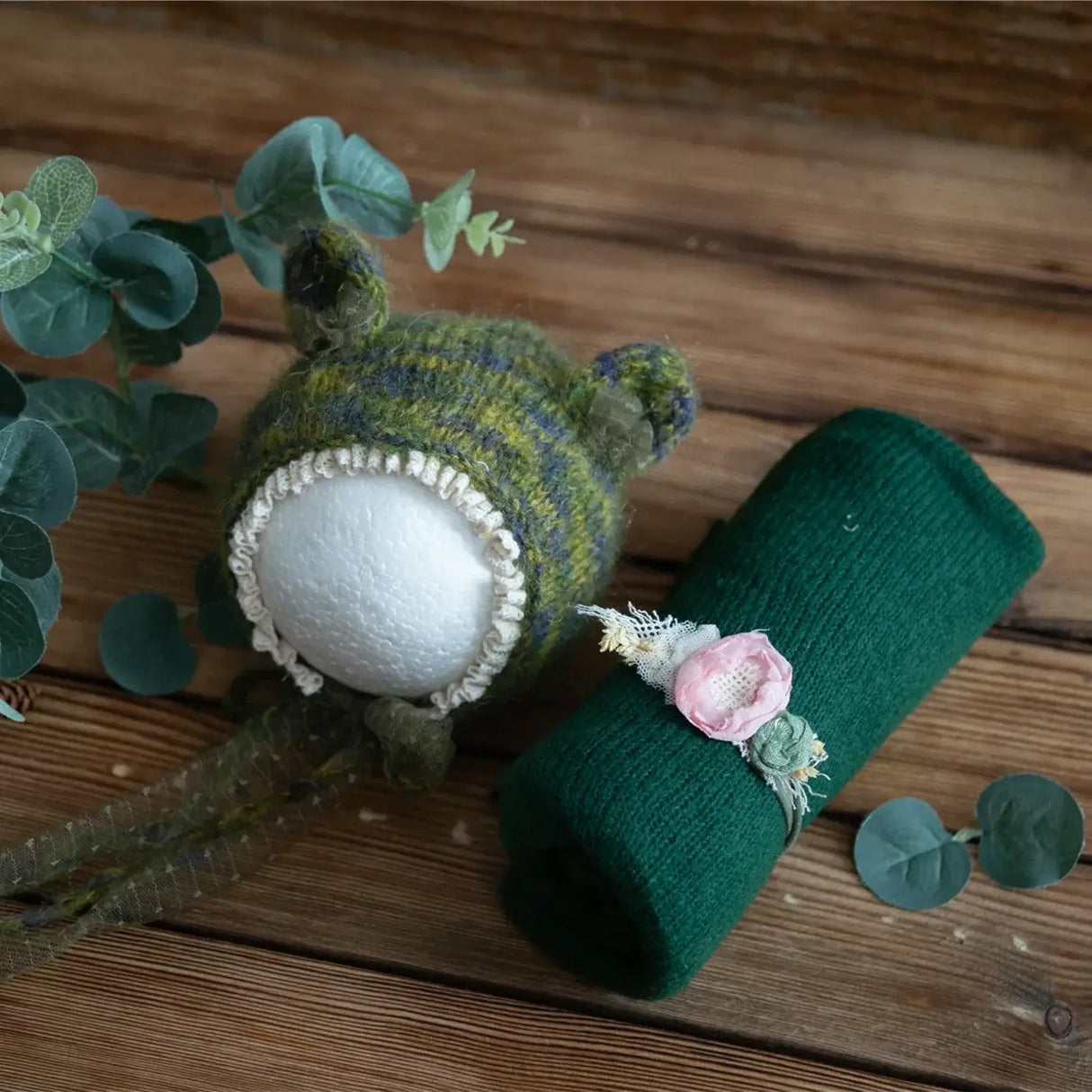 Newborn stretch knit mohair hat with ear details and matching wrap on a wooden surface, adorned with floral accents.