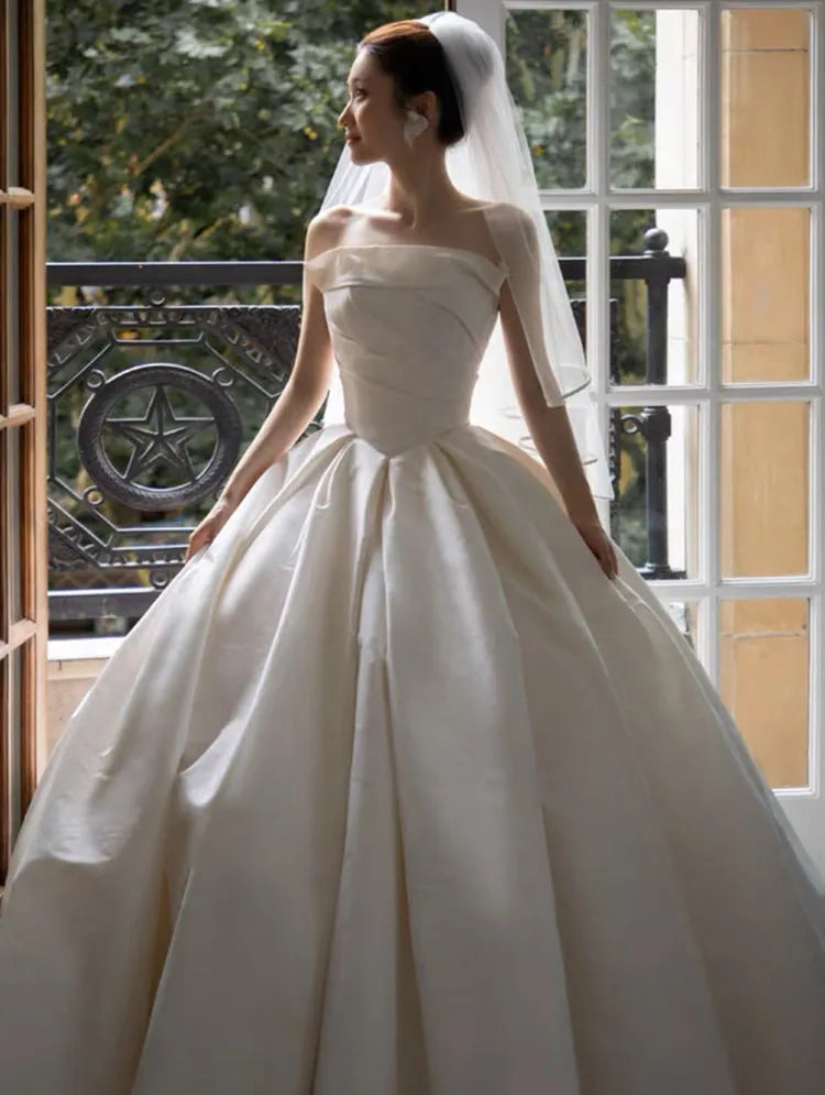 Elegant bride in a satin off-shoulder wedding gown with a full skirt, showcasing timeless bridal beauty and style.