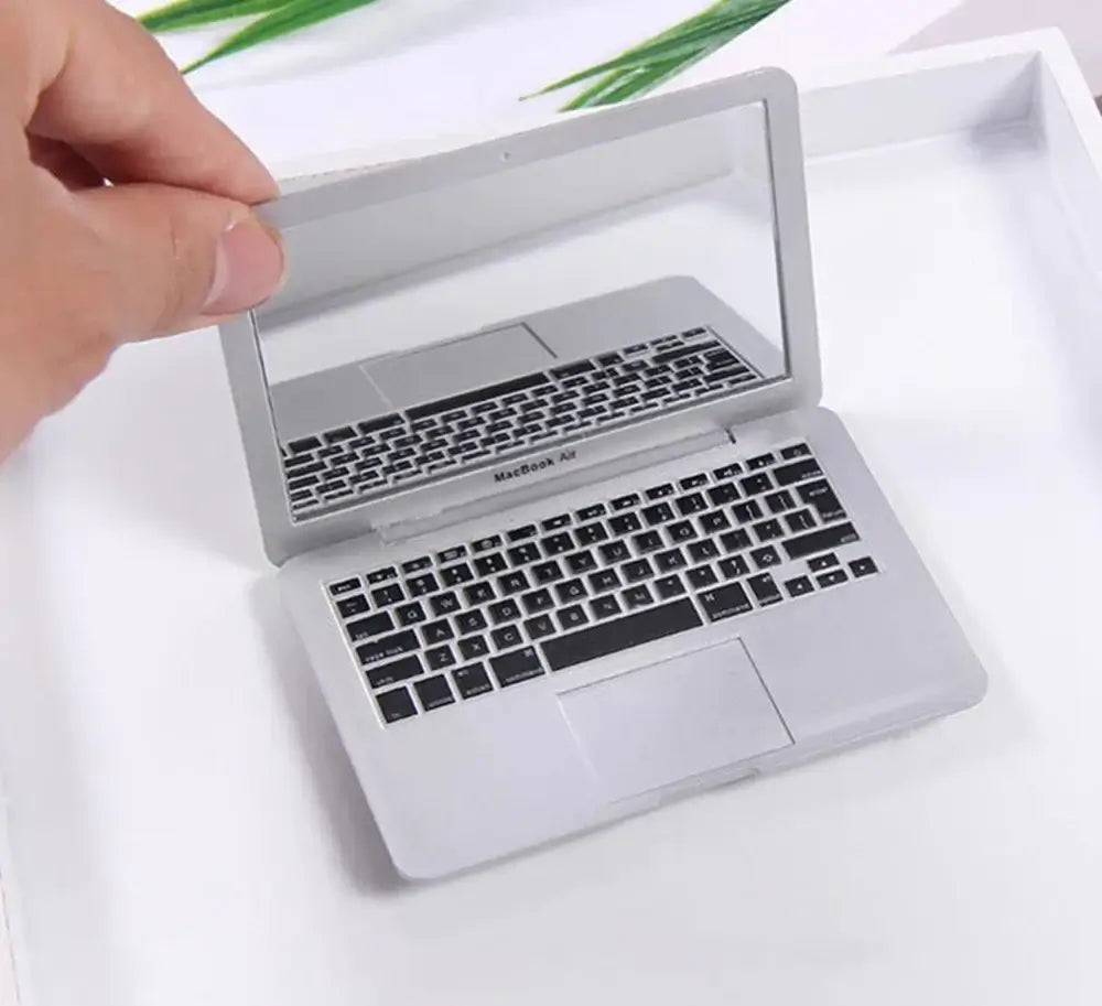 Hand holding a miniature silver laptop with a reflective screen, showcasing a detailed keyboard design.