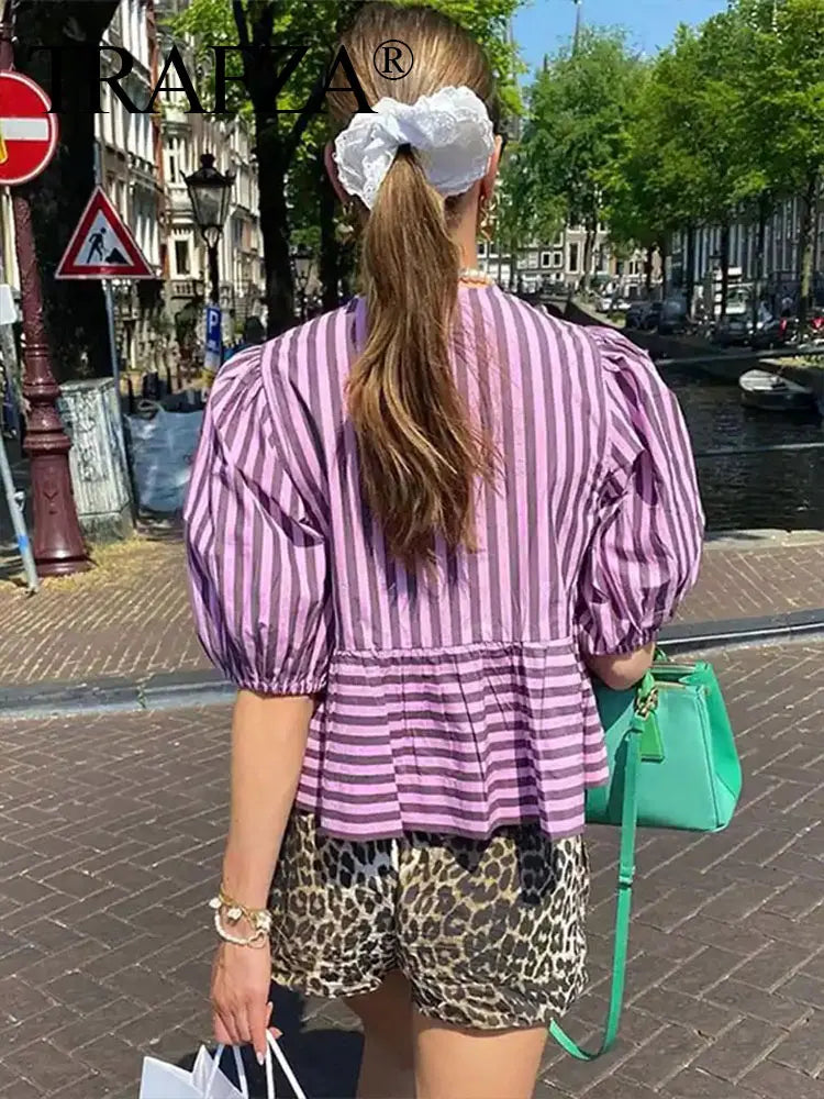 Woman wearing a striped lace-up blouse with puff sleeves, walking in a vibrant urban setting.