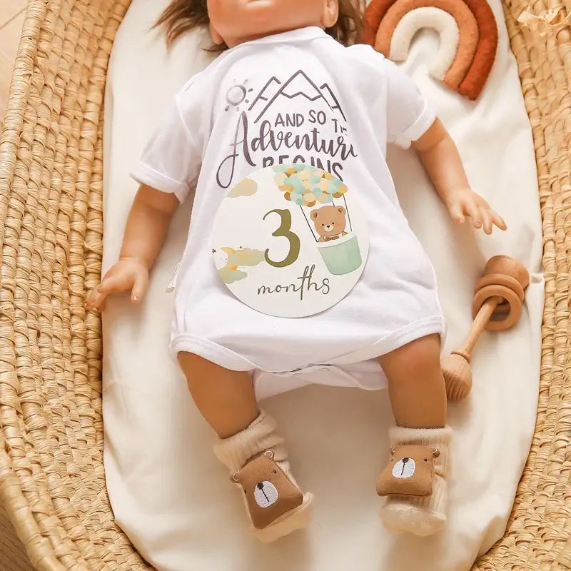Baby doll wearing a white onesie with '3 months' milestone and bear pattern, placed in a cozy basket.