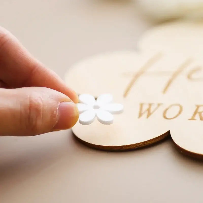 Hand placing a white flower on a wooden baby milestone sign, perfect for capturing precious moments.