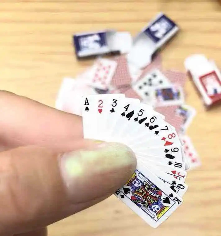 Close-up of a hand holding a fanned-out set of miniature playing cards on a wooden surface.